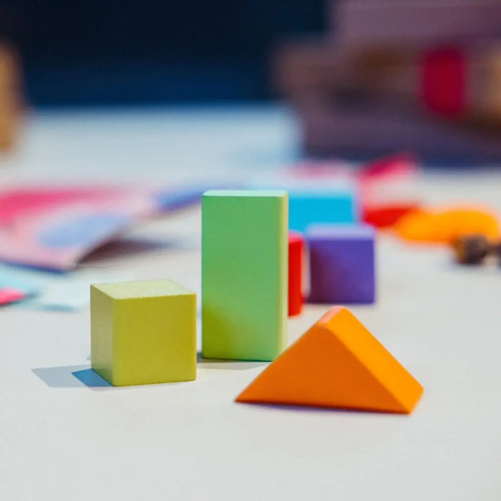 cubetti in legno da gioco: cubo giallo, piramide arancione, parallelepipedo verde chiaro
