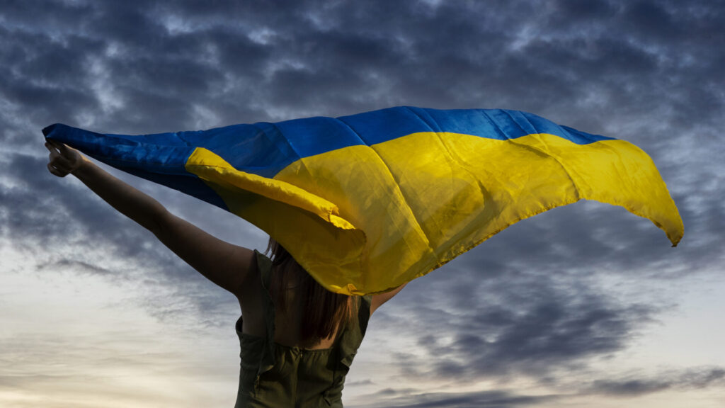 donna di spalle che tiene bandiera ucraina con cielo minaccioso
