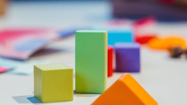 cubetti in legno da gioco: cubo giallo, piramide arancione, parallelepipedo verde chiaro