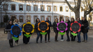 Foto di gruppo di insegnanti in cortile che tengono fiori colorati con messaggi che invitano a donare per il fundraising