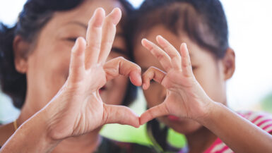 Asian grandmother and little child girl making heart shape with hands together with love