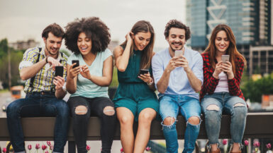 Multi-ethnic group of people sitting on an urban bridge text messaging and sharing smart phone content.